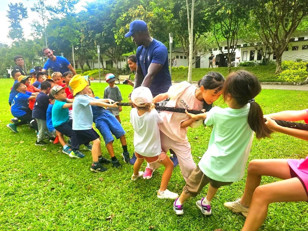 Children and coaches playing tug of war on the grass at KidsCamp Singapore, Fort Canning Park